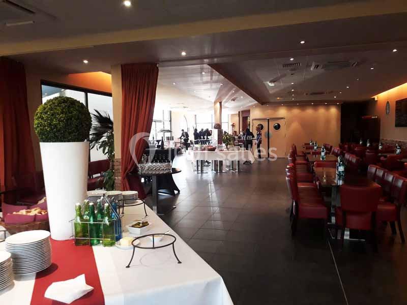 Salle de restaurant spacieuse avec tables dressées, chaises rouges et buffet en préparation au premier plan.