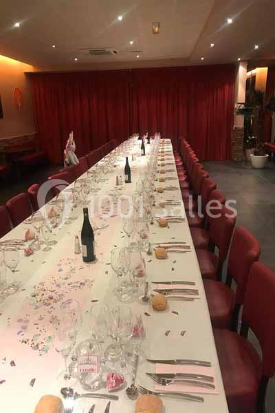 Grande table dressée pour un repas festif, avec nappes blanches, verres, couverts, bouteilles et décorations.