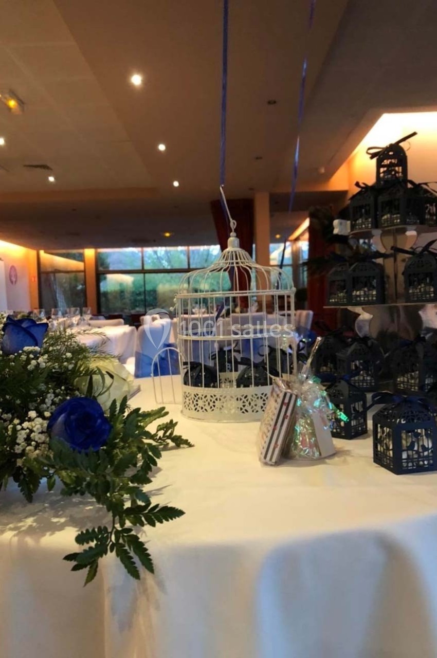 Décoration de table avec cage blanche, fleurs bleues et blanches, et petites lanternes noires dans une salle de réception.