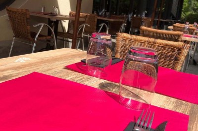 Terrasse de restaurant avec tables en bois, nappes rouges, couverts et verres, entourée de chaises en osier.