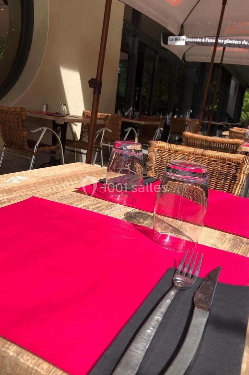 Terrasse de restaurant avec tables en bois, nappes rouges, couverts et verres, entourée de chaises en osier.