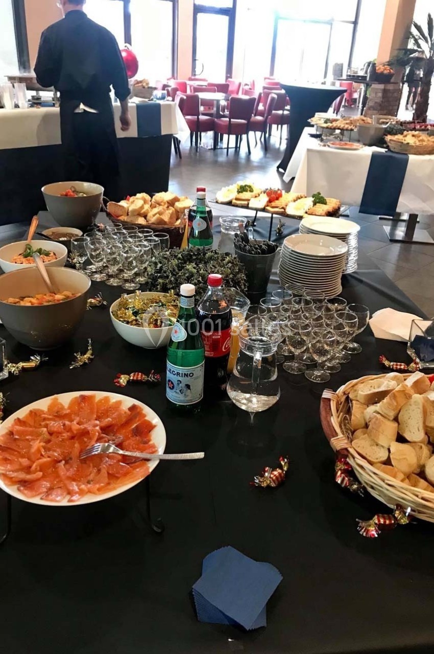 Buffet varié avec saumon fumé, salades, pains et boissons, disposé sur une table dans une salle lumineuse.