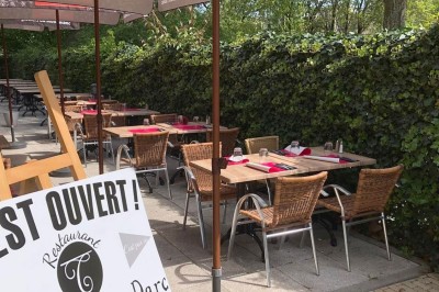 Terrasse de restaurant avec tables en bois, nappes rouges, couverts et verres, entourée de chaises en osier.