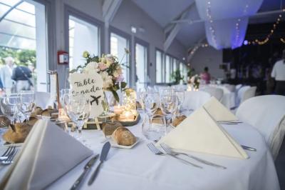 Maison blanche à étage avec escalier extérieur en bois, cabanon en bois à côté, jardin fleuri et clôture en bois.
