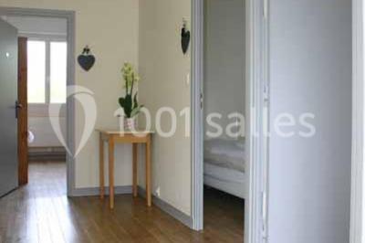 Vue d'un couloir lumineux menant à une chambre avec un lit, des murs clairs et un tapis au sol.