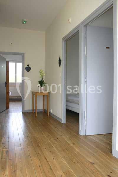 Couloir lumineux avec parquet en bois, table avec plante et portes ouvertes menant à des pièces.