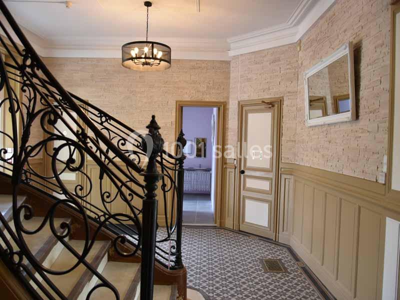 Escalier en fer forgé dans un hall d'entrée lumineux avec murs en pierre, carrelage au sol et miroir mural.