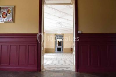 Vue d'un couloir lumineux menant à une chambre avec un lit, des murs clairs et un tapis au sol.