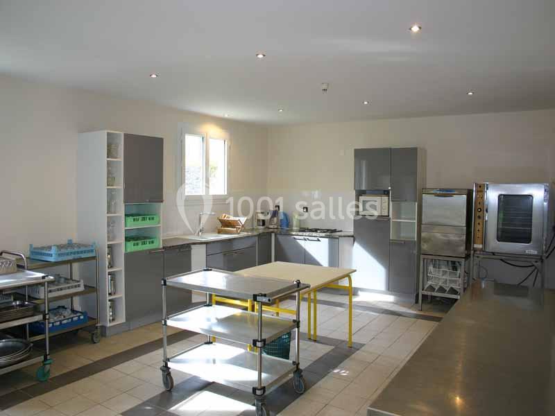 Cuisine professionnelle lumineuse avec équipements modernes, tables en inox sur roulettes et appareils électroménagers.