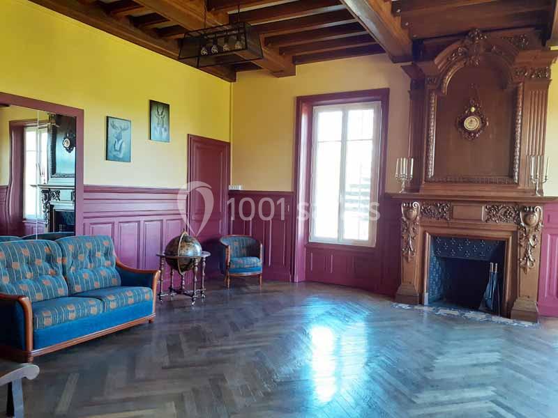 Salon avec parquet en bois, cheminée décorative, canapé, fauteuils, globe terrestre et murs jaunes et rouges.