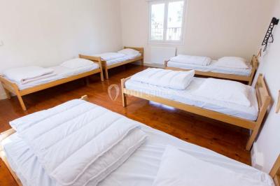 Vue d'un couloir lumineux menant à une chambre avec un lit, des murs clairs et un tapis au sol.