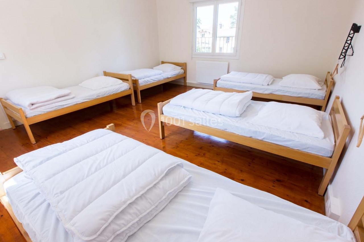 Chambre lumineuse avec cinq lits simples en bois, draps blancs et parquet au sol.