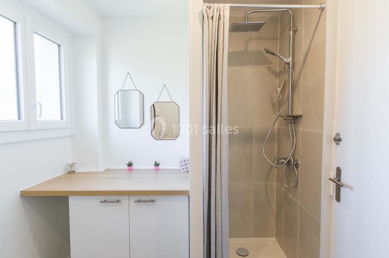 Salle de bain avec douche à l'italienne, meuble avec plan en bois, deux miroirs et petites plantes décoratives.