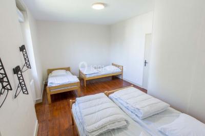 Vue d'un couloir lumineux menant à une chambre avec un lit, des murs clairs et un tapis au sol.