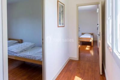 Vue d'un couloir lumineux menant à une chambre avec un lit, des murs clairs et un tapis au sol.