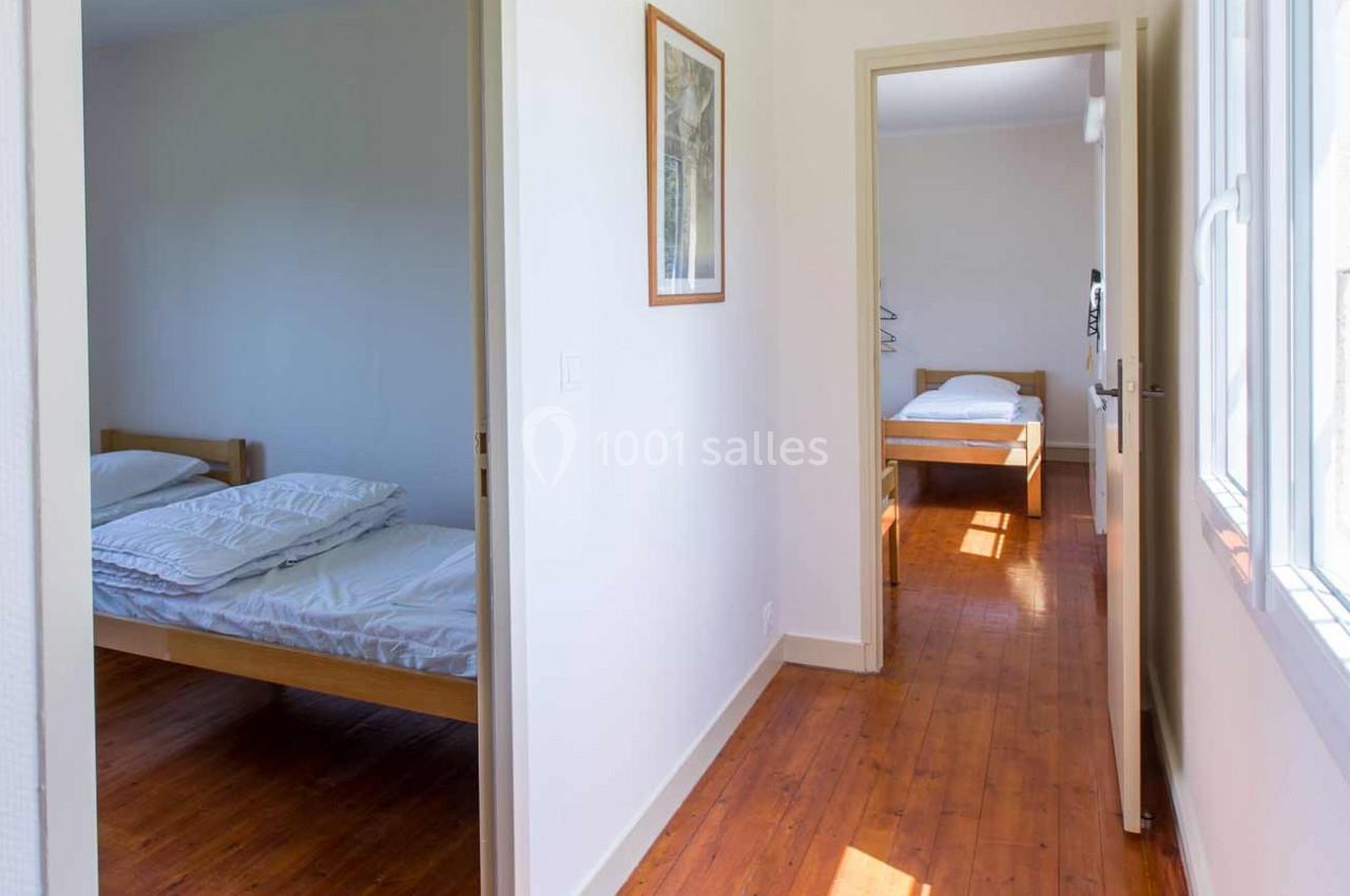 Deux chambres lumineuses avec lits simples, parquet au sol et murs blancs, reliées par un couloir ouvert.