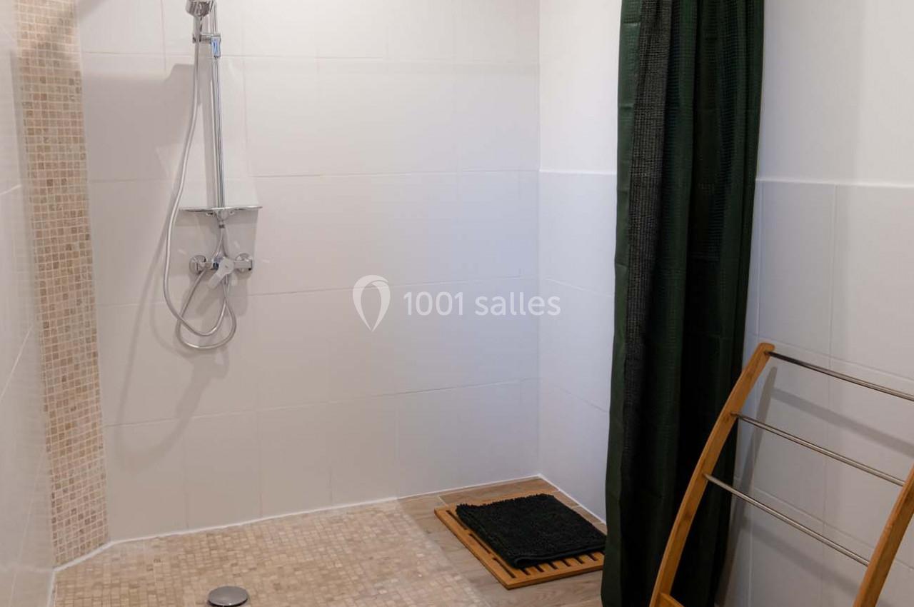 Douche à l'italienne avec carrelage beige, rideau vert, tapis en bois et porte-serviettes en bois.
