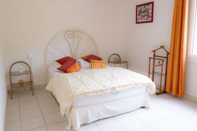 Vue d'un couloir lumineux menant à une chambre avec un lit, des murs clairs et un tapis au sol.