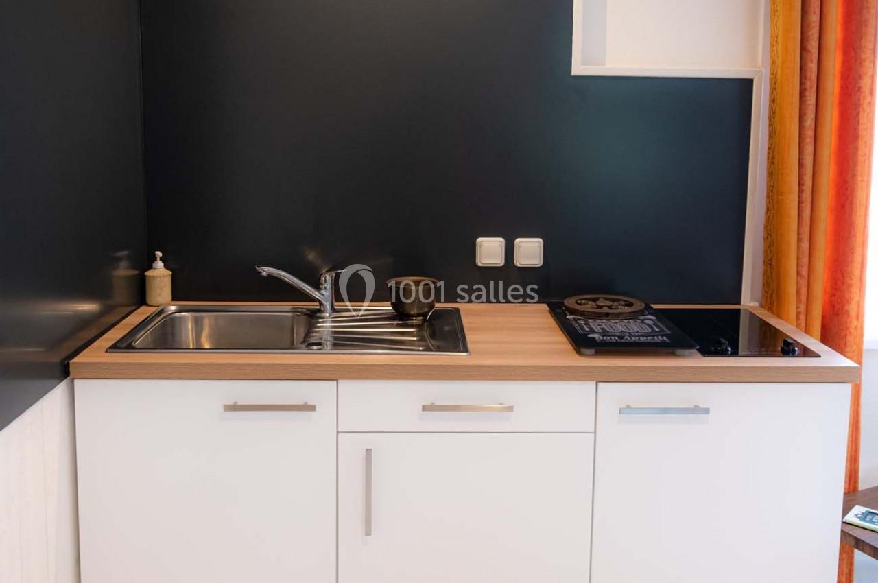 Cuisine compacte avec évier en inox, plaque de cuisson noire, plan de travail en bois clair et mur sombre.