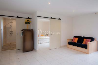 Vue d'un couloir lumineux menant à une chambre avec un lit, des murs clairs et un tapis au sol.