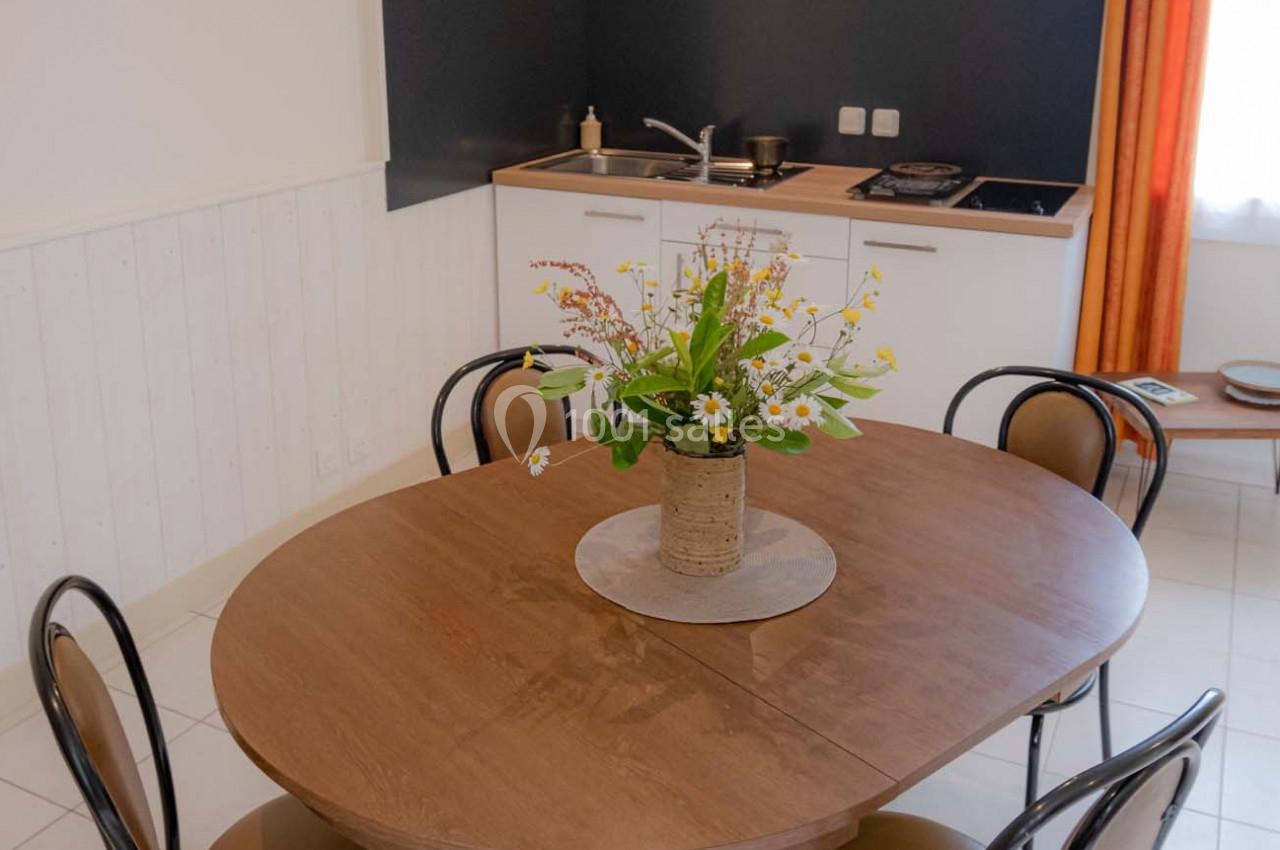 Table ronde en bois avec un bouquet de fleurs au centre, située dans une cuisine équipée avec évier et plaques de cuisson.