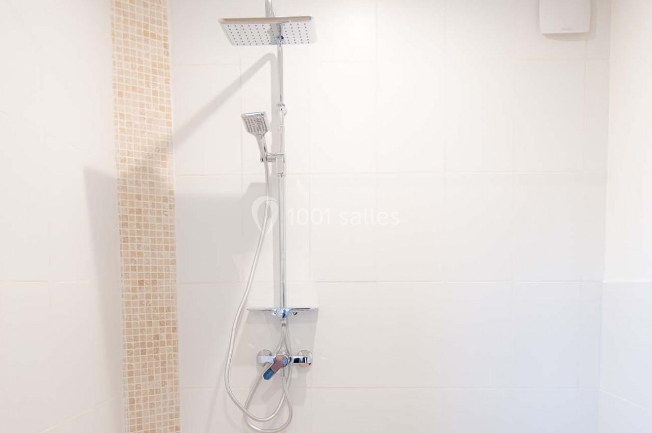 Douche moderne avec colonne équipée d'une pomme haute et d'une douchette, mur carrelé partiellement en mosaïque beige.