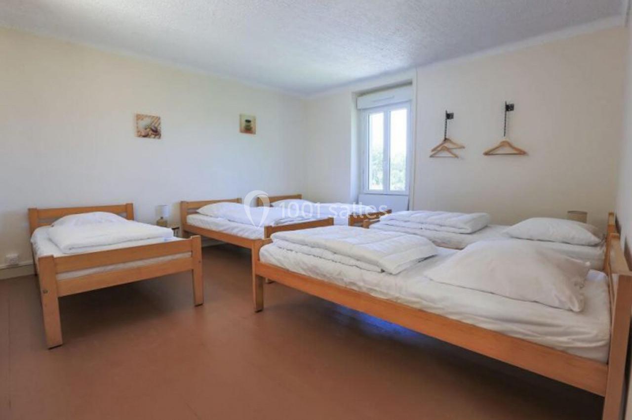 Quatre lits simples en bois avec draps blancs dans une chambre lumineuse équipée de cintres et décorations murales.