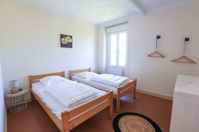 Vue d'un couloir lumineux menant à une chambre avec un lit, des murs clairs et un tapis au sol.