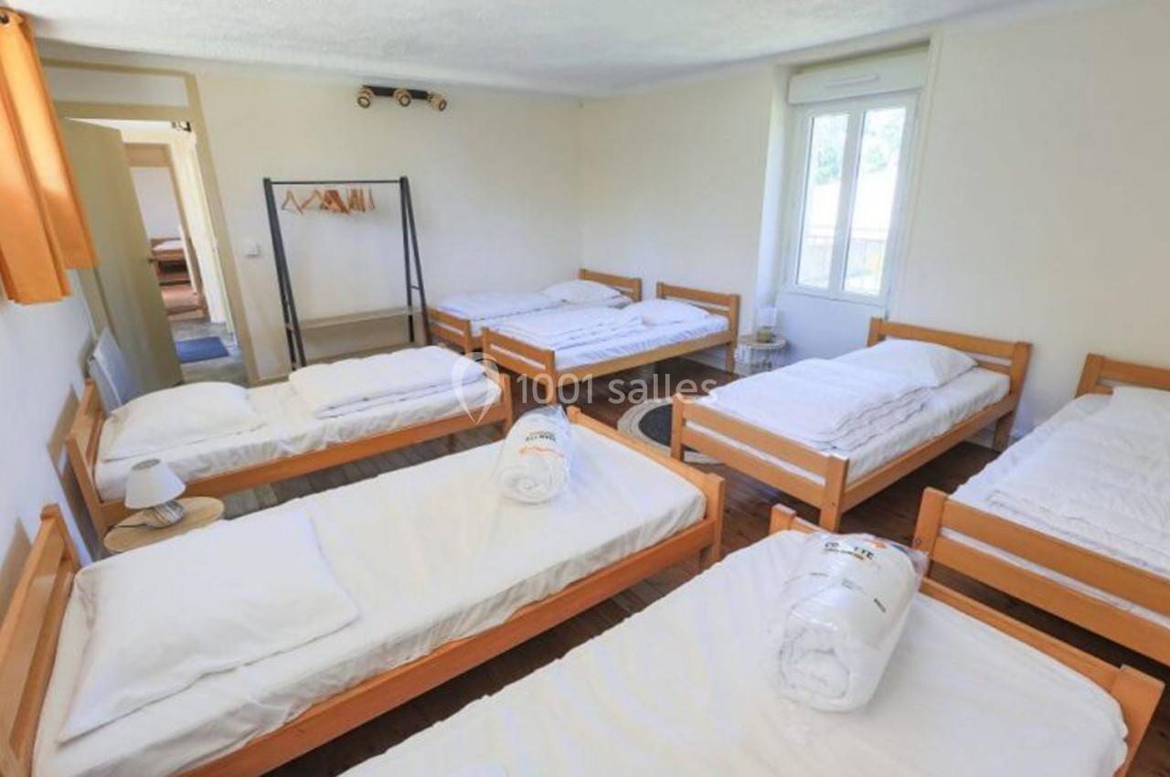 Chambre lumineuse avec six lits simples en bois, linge de lit blanc et portant avec cintres.