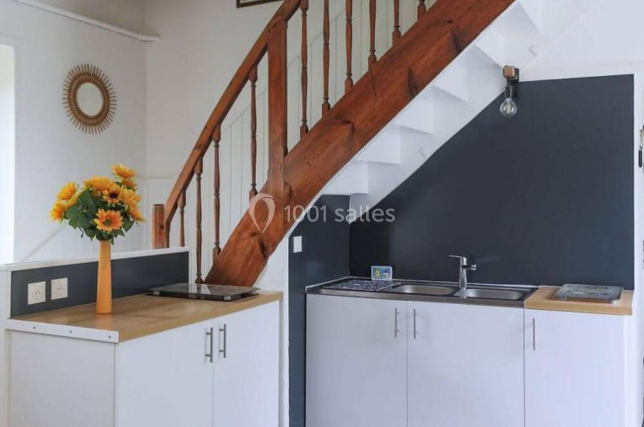 Cuisine compacte avec meubles blancs, plan de travail en bois, évier inox et escalier en bois au-dessus.