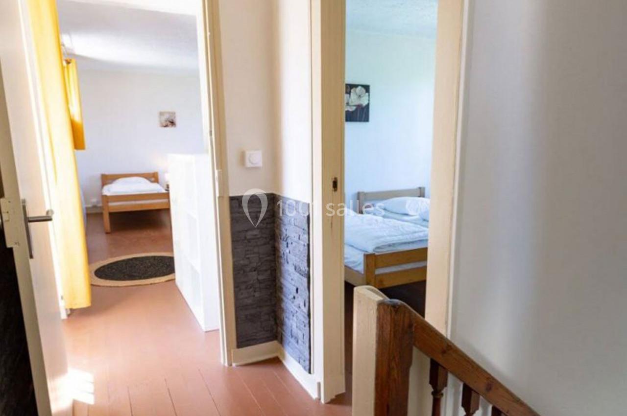 Vue d'un couloir donnant sur deux chambres lumineuses avec lits simples et parquet au sol.