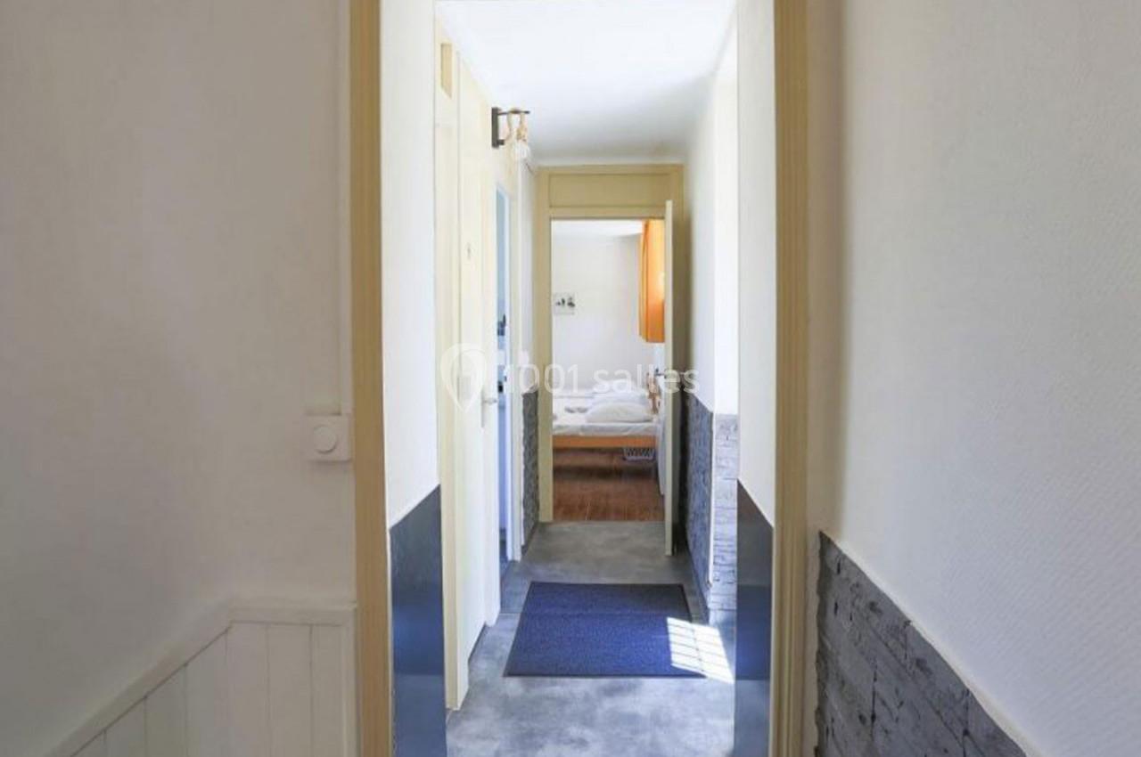 Vue d'un couloir lumineux menant à une chambre avec un lit, des murs clairs et un tapis au sol.