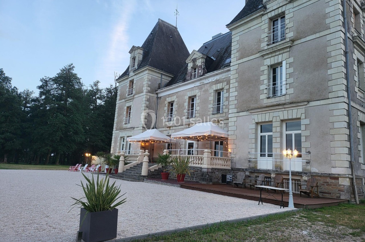 Façade d'un château ancien avec terrasse aménagée, éclairages et mobilier extérieur, entouré de végétation.