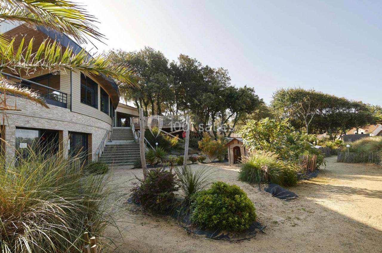 Jardin paysager avec végétation méditerranéenne, escaliers menant à une maison moderne entourée d'arbres.