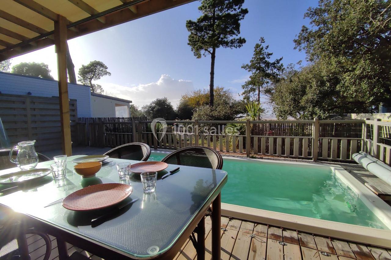 Table dressée en extérieur sur une terrasse en bois, près d'une piscine, entourée de végétation et clôturée.
