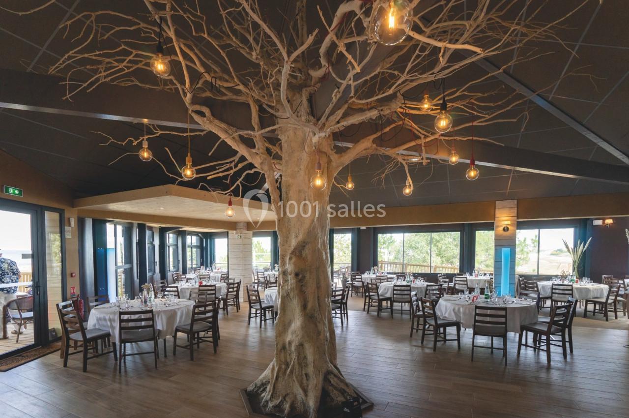 Salle de restaurant avec un grand arbre décoratif au centre et des tables dressées autour.