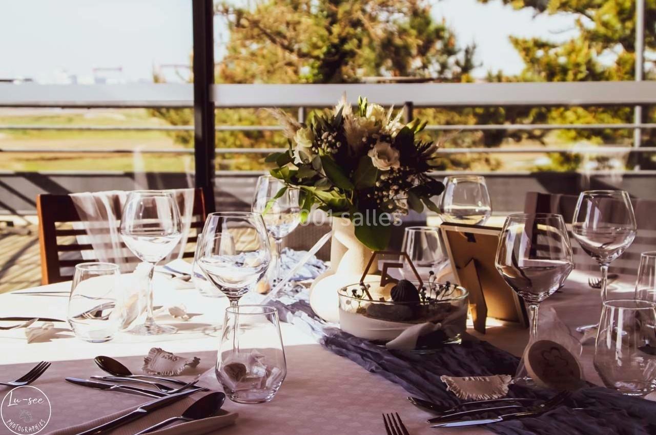 Table dressée avec vaisselle élégante, bouquet de fleurs au centre, lumière naturelle et vue sur l'extérieur.