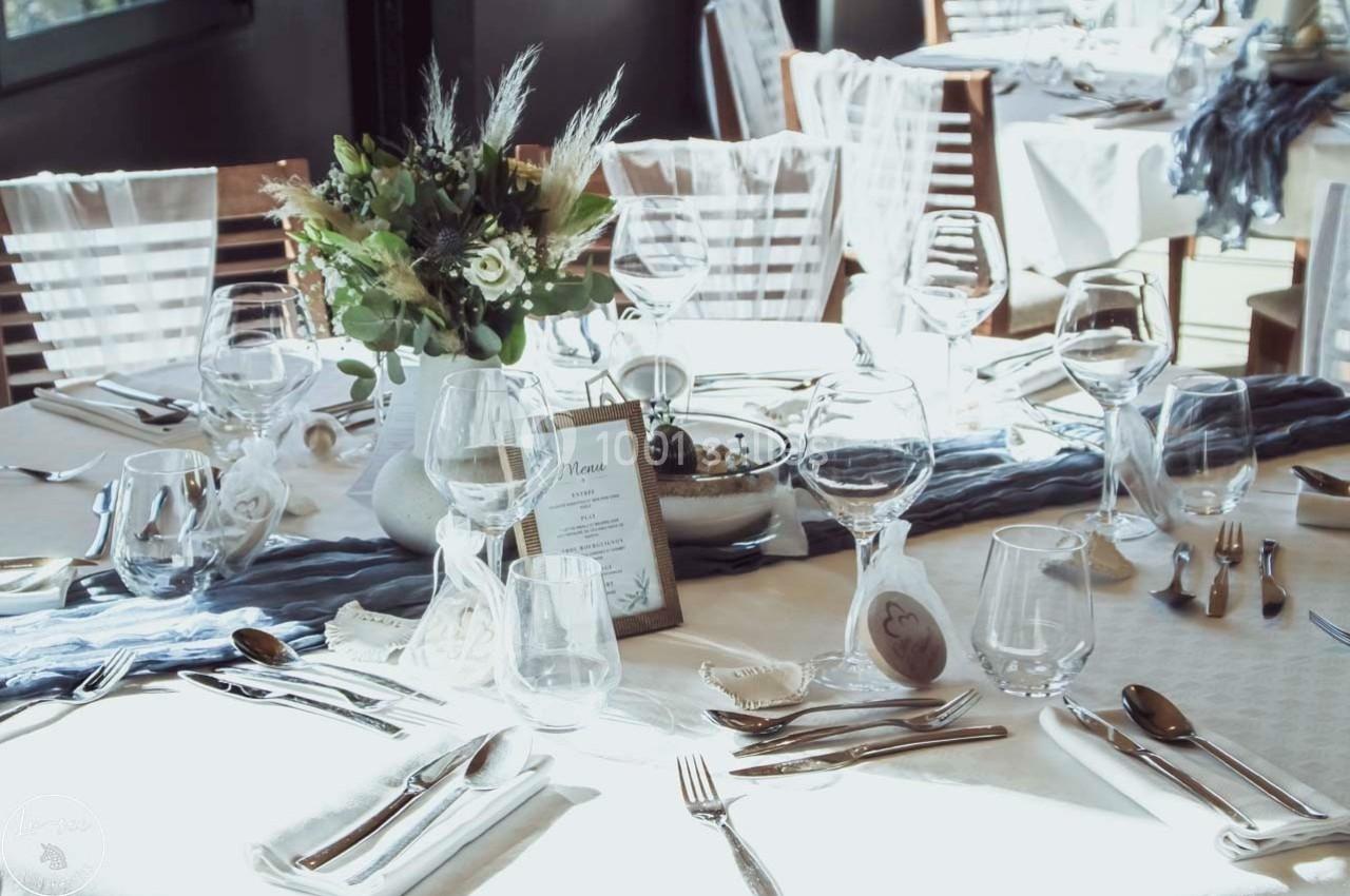 Table élégamment dressée avec vaisselle, verres, menu et centre de table floral dans une ambiance lumineuse.