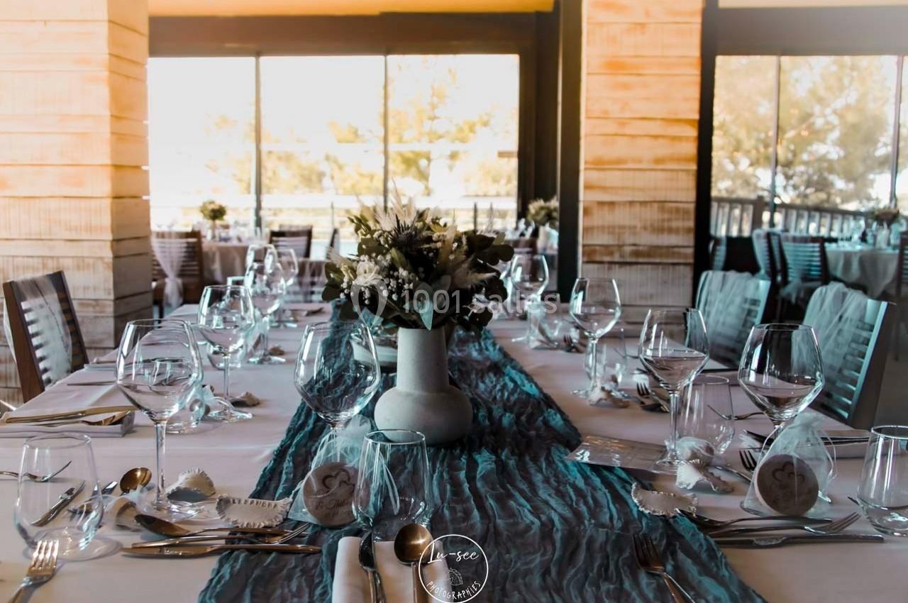 Table dressée pour un repas avec nappes blanches, chemins de table bleus, vaisselle élégante et bouquet central.