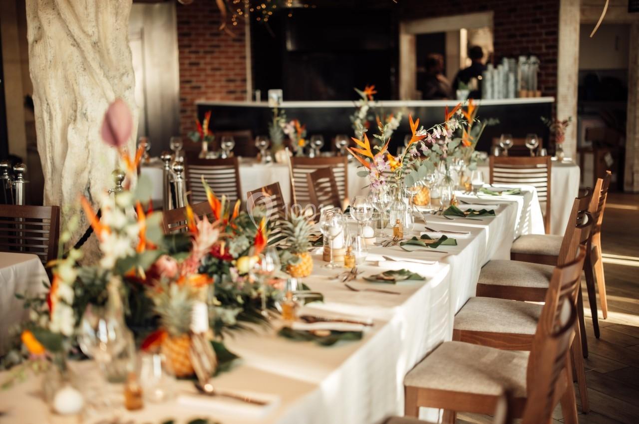 Salle de réception décorée avec des tables dressées, ornées de fleurs tropicales et de vaisselle élégante.