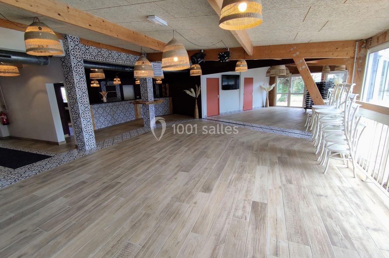 Salle lumineuse avec parquet en bois, comptoir décoré de motifs, chaises empilées et suspensions en osier.