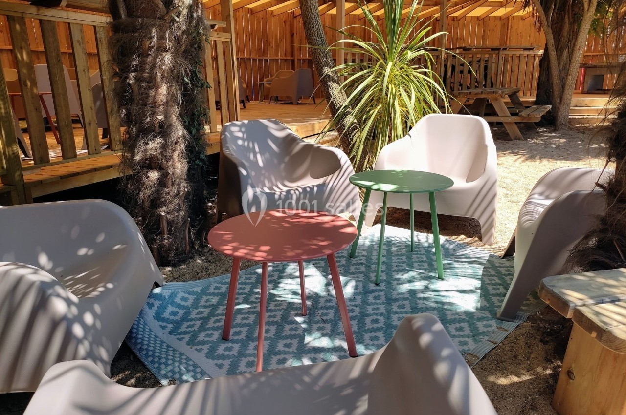 Mobilier de jardin avec fauteuils et tables colorées sur un tapis, entouré de végétation et d'une structure en bois.