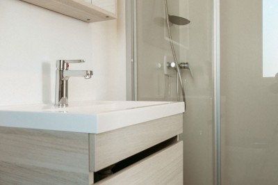 Salle de bain moderne avec meuble en bois clair, lavabo, miroir et douche vitrée équipée d'une pomme de douche.