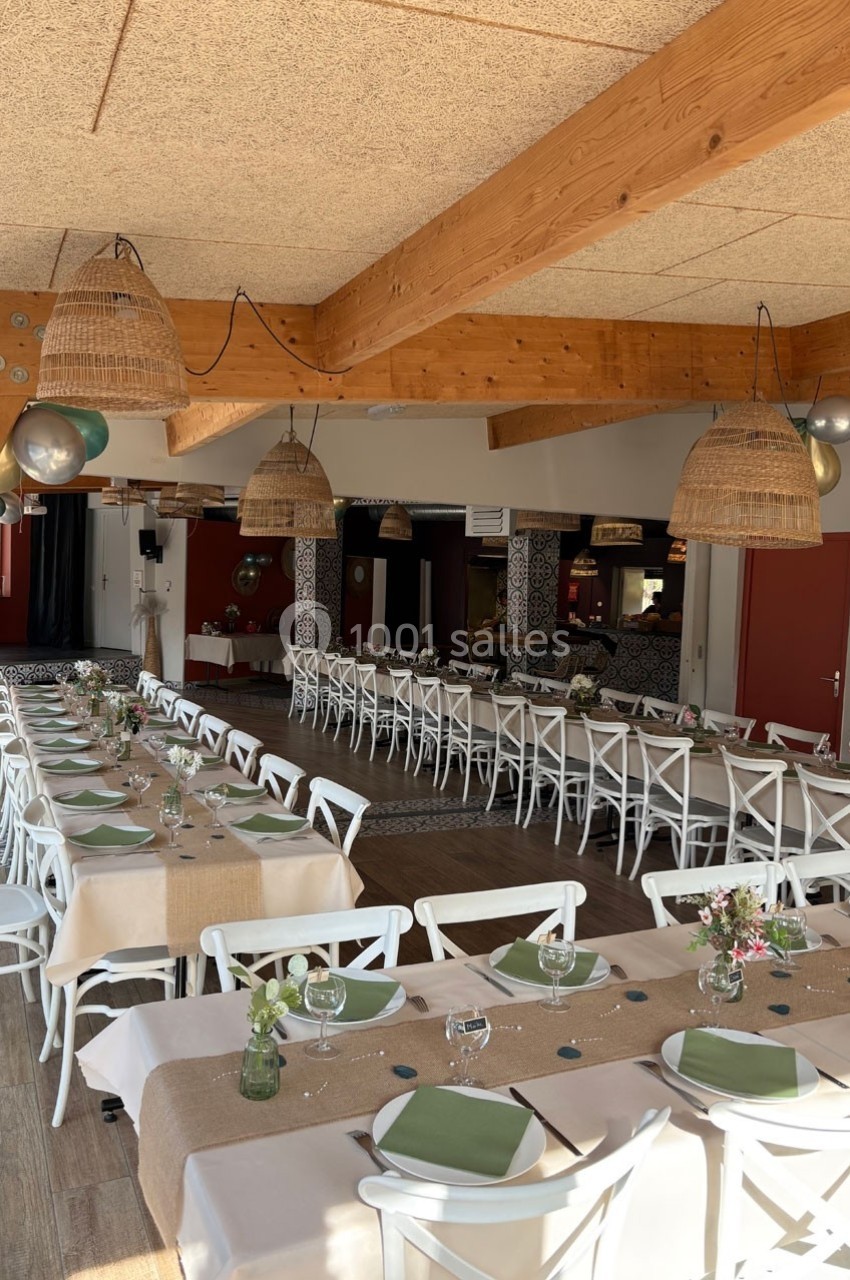 Salle de réception lumineuse avec tables dressées, nappes beige, assiettes vertes et décoration florale.