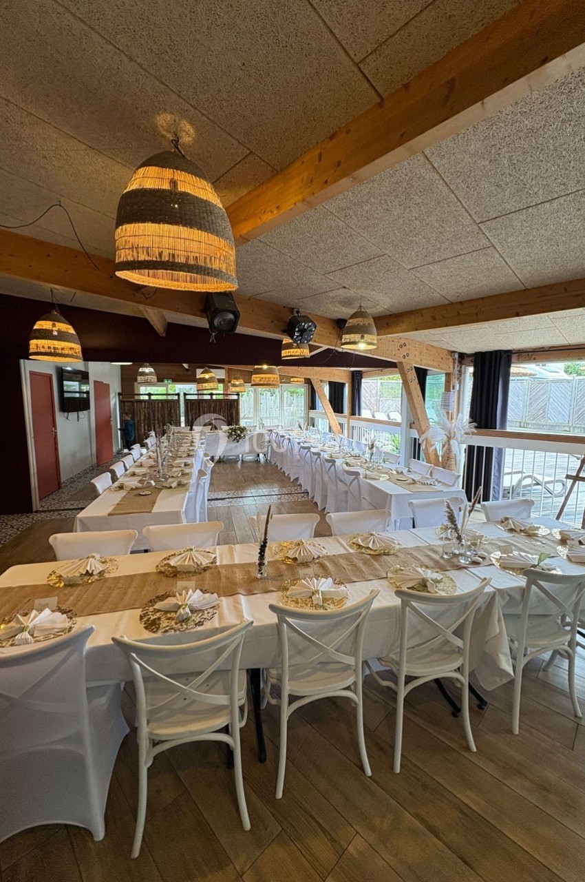 Salle de réception décorée avec de longues tables dressées, nappes blanches et éclairage suspendu en osier.