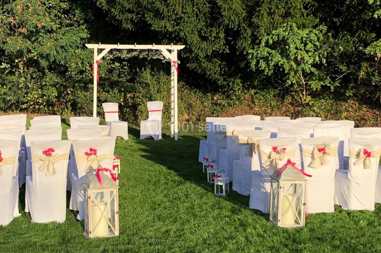 Chaises blanches décorées de rubans rouges disposées en extérieur devant une arche de mariage en bois.