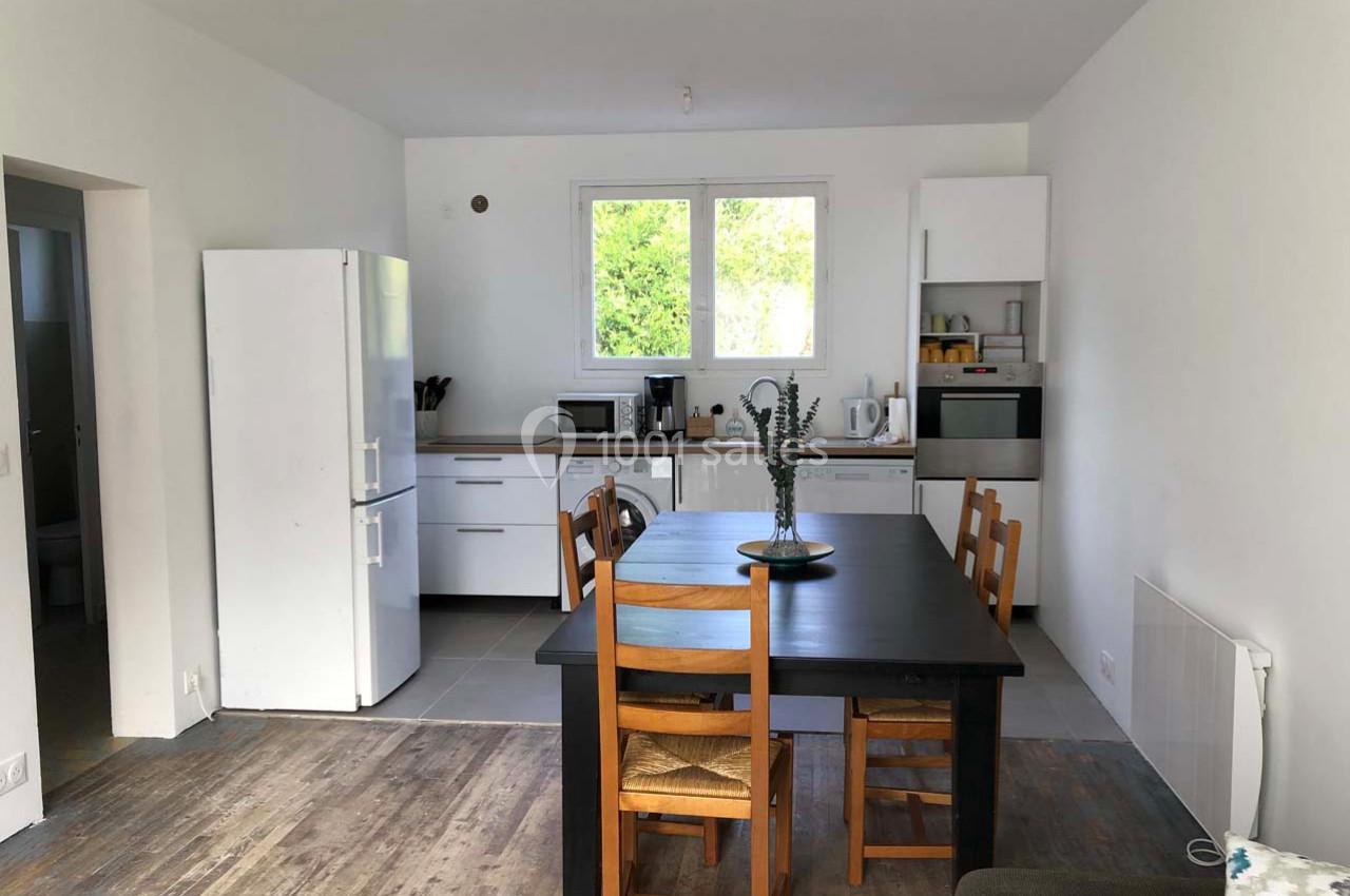 Cuisine moderne avec table en bois foncé, chaises, réfrigérateur, four, micro-ondes et fenêtre donnant sur un jardin.