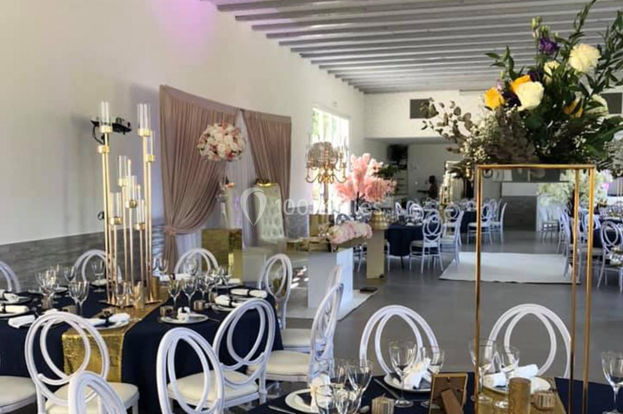 Salle de réception décorée avec des tables dressées, des chaises blanches et des arrangements floraux élégants.