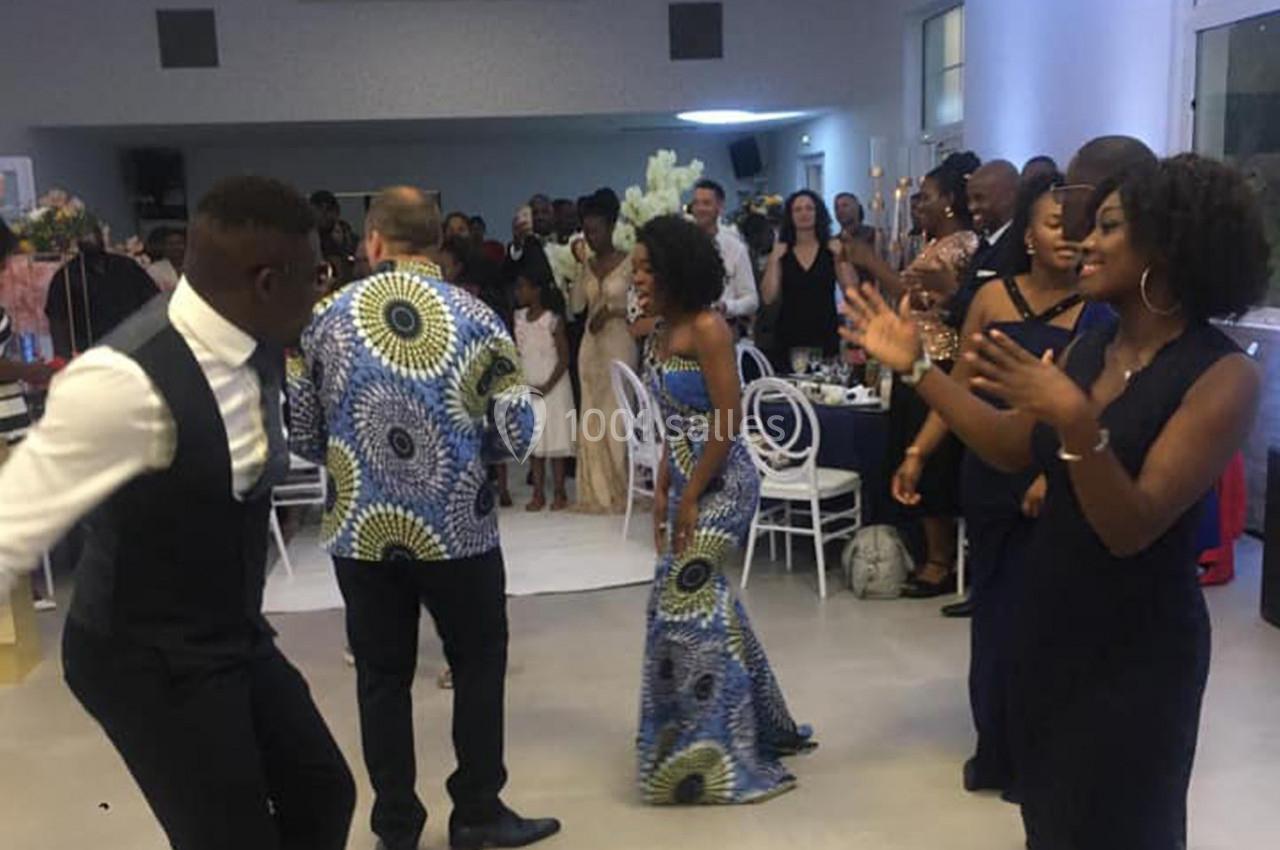 Des personnes dansent et applaudissent lors d'une fête, dans une salle lumineuse avec des invités en arrière-plan.