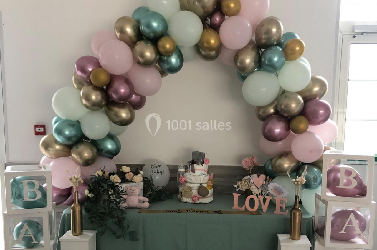 Arc de ballons pastel décorant une table avec des cadeaux, un gâteau de couches et des éléments sur le thème de la naissance.